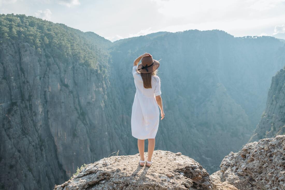 Woman standing on a cliff's edge looking into a mountainous valley.
