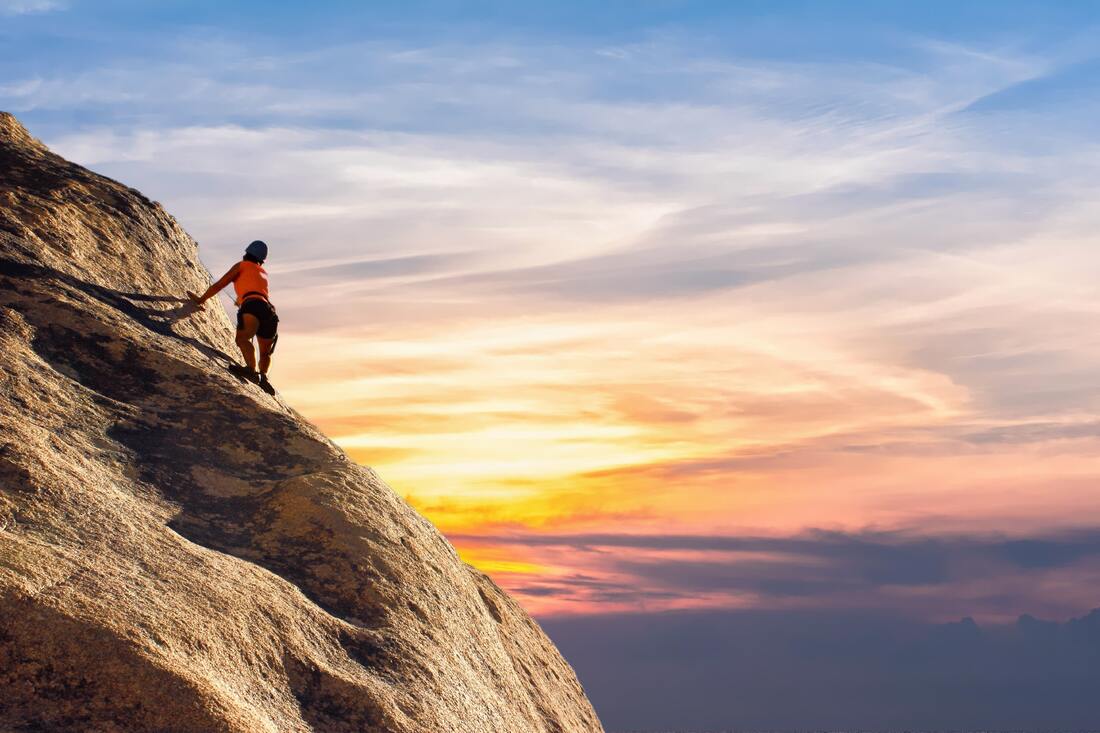 Person climbing a mountain cliff with a lovely sunrise behind them