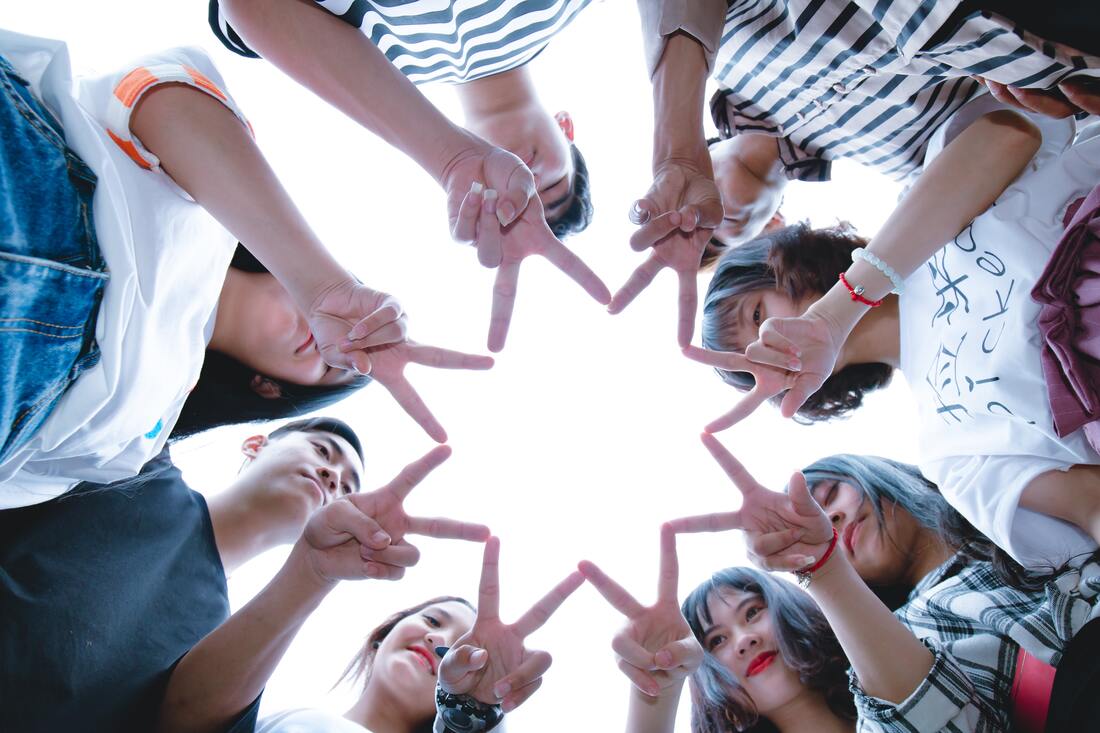 Looking up at people in a circle putting their fingers together to form the shape of an 8-pointed star.
