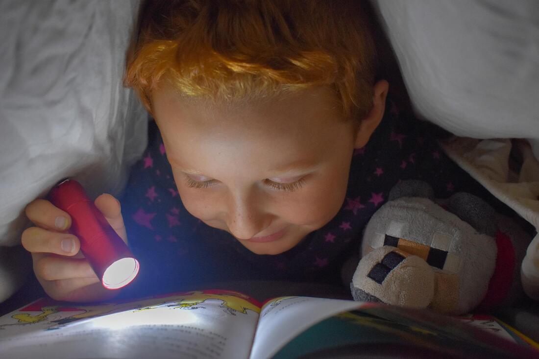 Little boy eagerly reading a book past his bedtime.